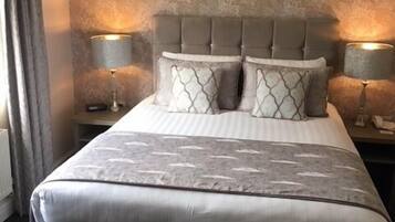 A large bed with a tufted headboard, two bedside lamps, and a patterned bedspread.