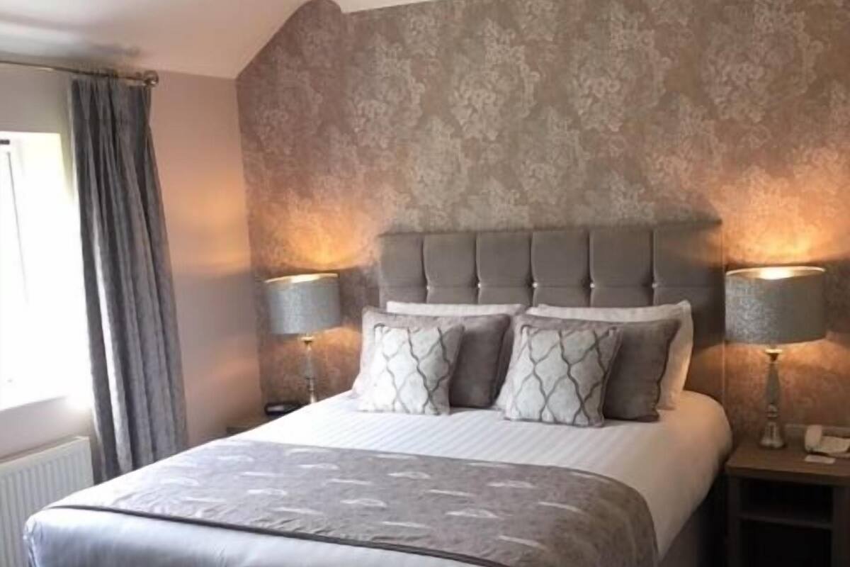 A bedroom with a large bed, two bedside tables with lamps, a patterned wall, and a window with curtains.