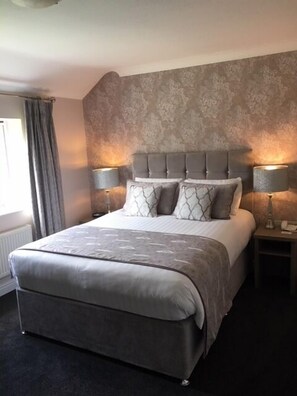 A bedroom with a large bed, two bedside tables with lamps, a patterned wall, and a window with curtains.