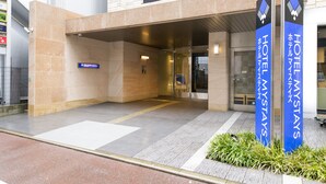 Entrada de un hotel con un letrero que dice "HOTEL MYSTAYS" y una señal azul que indica la ubicación.