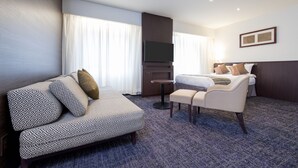 Una habitación de hotel con sofá, cama, televisor y una mesita.