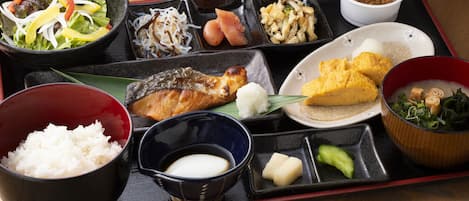 Comida tradicional japonesa servida en una bandeja negra con diversos platos, incluyendo arroz, pescado y verduras.