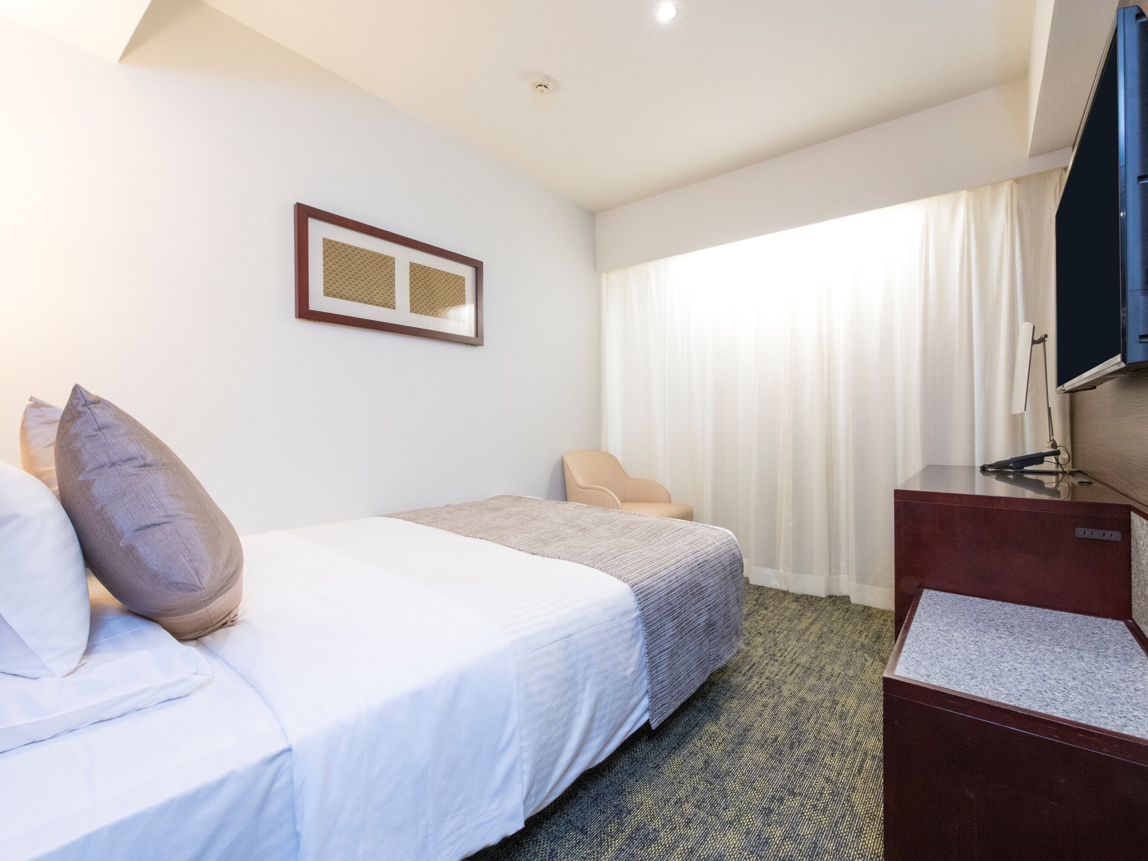 A hotel room with two beds, a desk, a TV, and a window with curtains.
