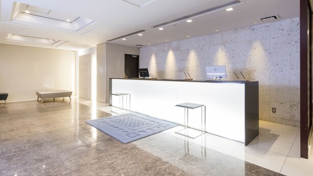 Un área de recepción moderna con suelo de mármol, una mesa de recepción, dos taburetes de bar y una alfombra estampada.