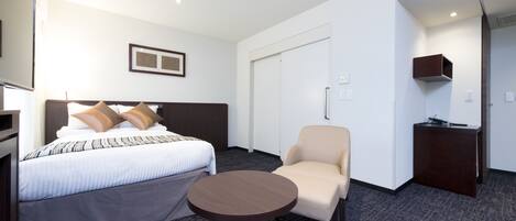 A hotel room with a bed, a round table, a chair, a desk, and a wardrobe.