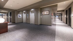 Un pasillo moderno de hotel con piso alfombrado, varias puertas y un mostrador de recepción.