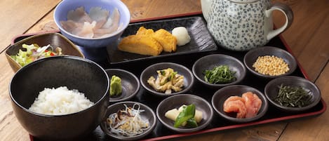 Un conjunto de comida tradicional japonesa sobre una mesa de madera, que incluye arroz, pescado, verduras y una tetera.