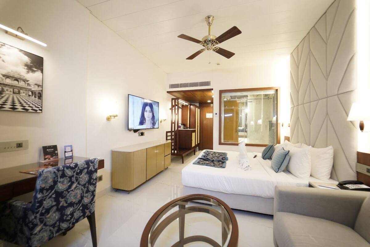 Una habitación de hotel moderna con cama, sofá, televisor, escritorio y ventilador de techo.
