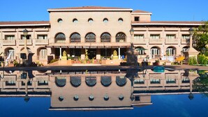 Un edificio grande con una piscina reflectante al frente, con ventanas arqueadas y una estatua central.