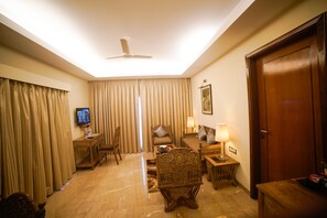 A well-lit living room with a ceiling fan, a television, and a wooden sofa set. - Evershine Resort & Spa (Mahabaleshwar)