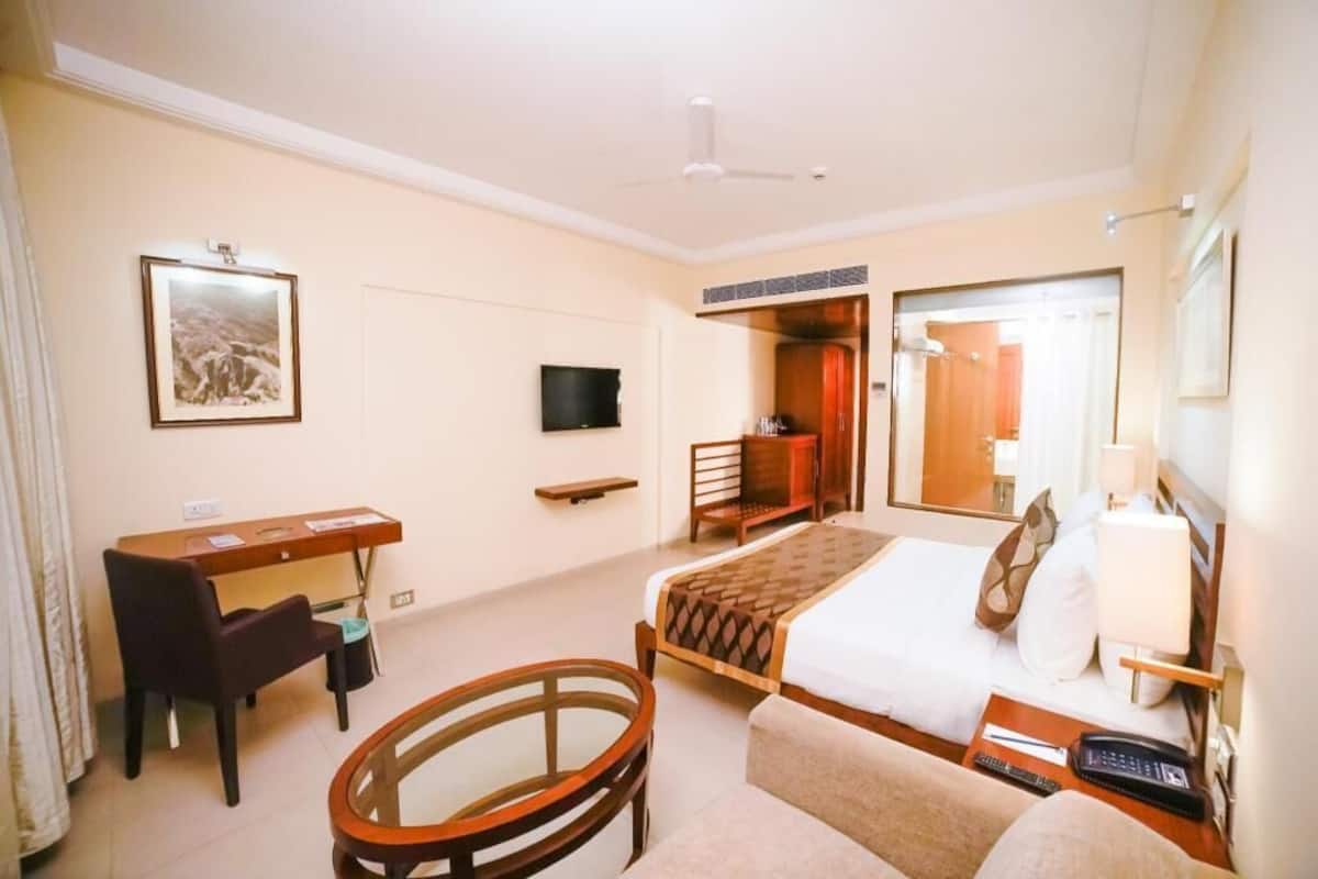 Habitación de hotel con cama, escritorio, silla, televisor y espejo.