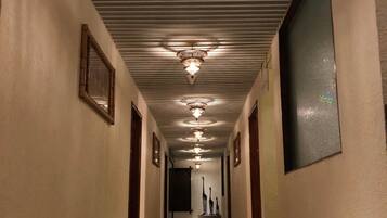 A long, narrow hallway with a reflective floor, multiple chandeliers, and framed pictures on the walls.