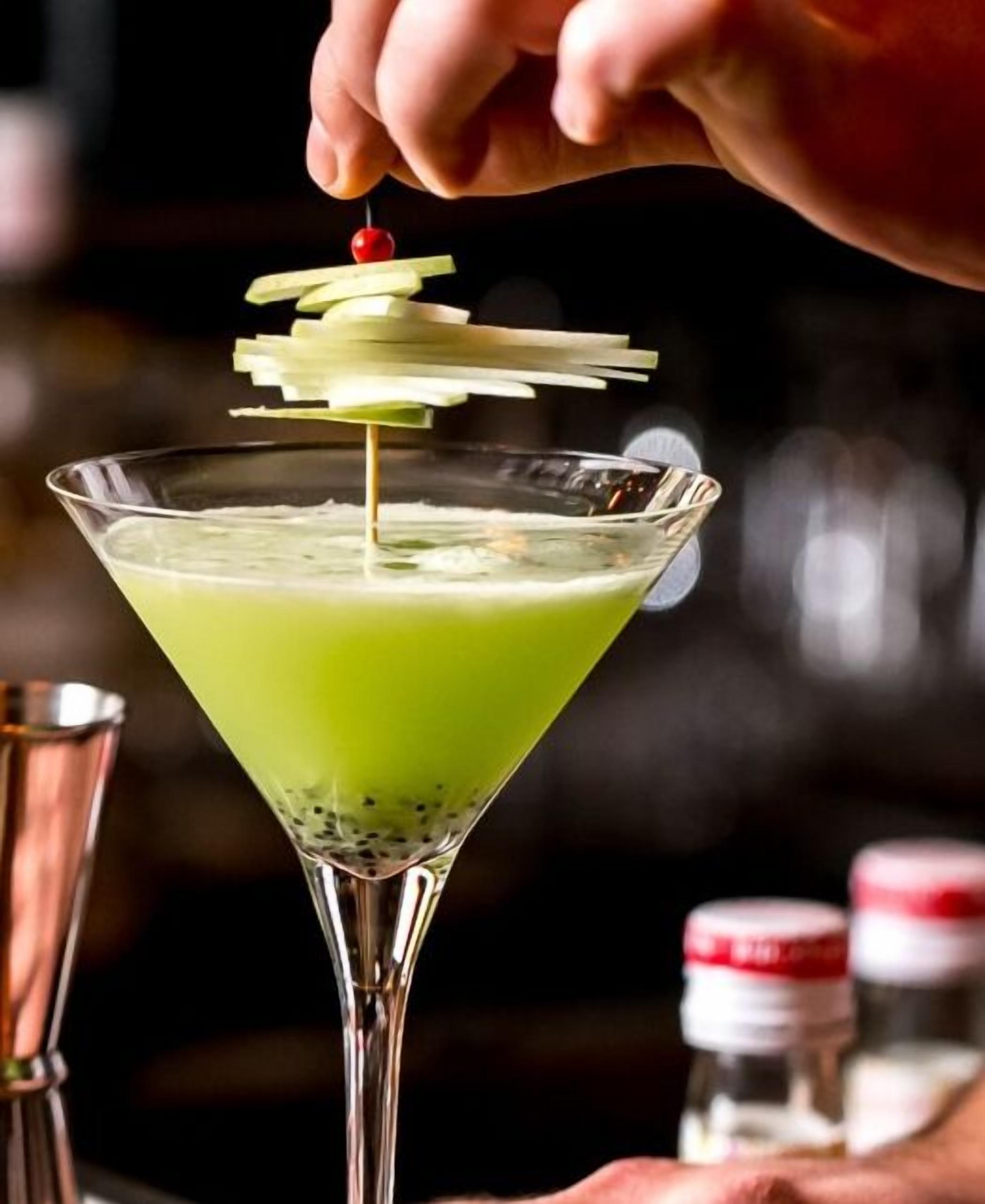 A martini glass with a green liquid and a cherry garnish.
