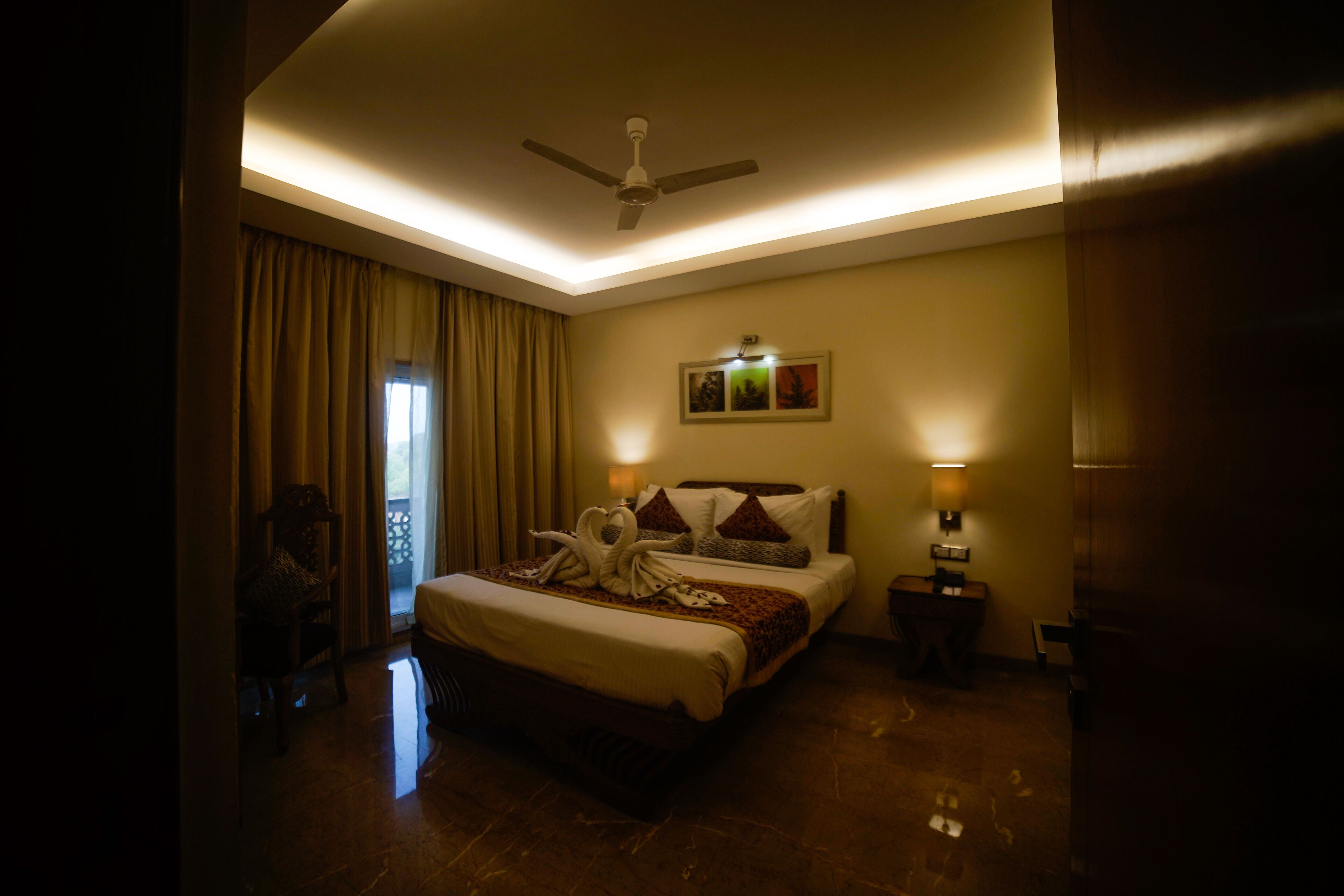 A hotel room with a bed, a ceiling fan, a nightstand, and a wall-mounted lamp.