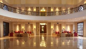 Un vestíbulo amplio con techo alto, una zona de estar central con cojines rojos y una barandilla decorativa.