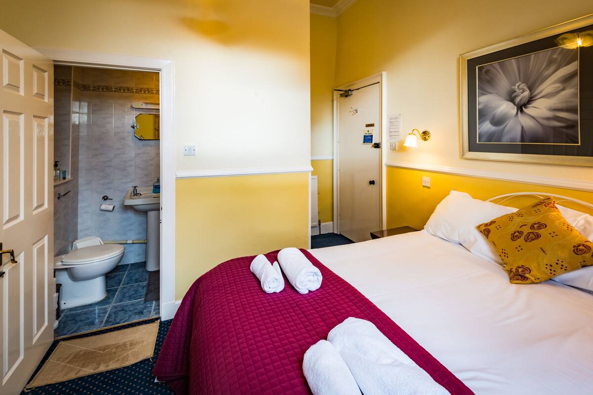 A hotel room with a bed, a bathroom, and a door leading to another room.