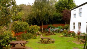 Un jardín bien cuidado con una mesa de picnic de madera, un pequeño estanque y diversas plantas y flores.