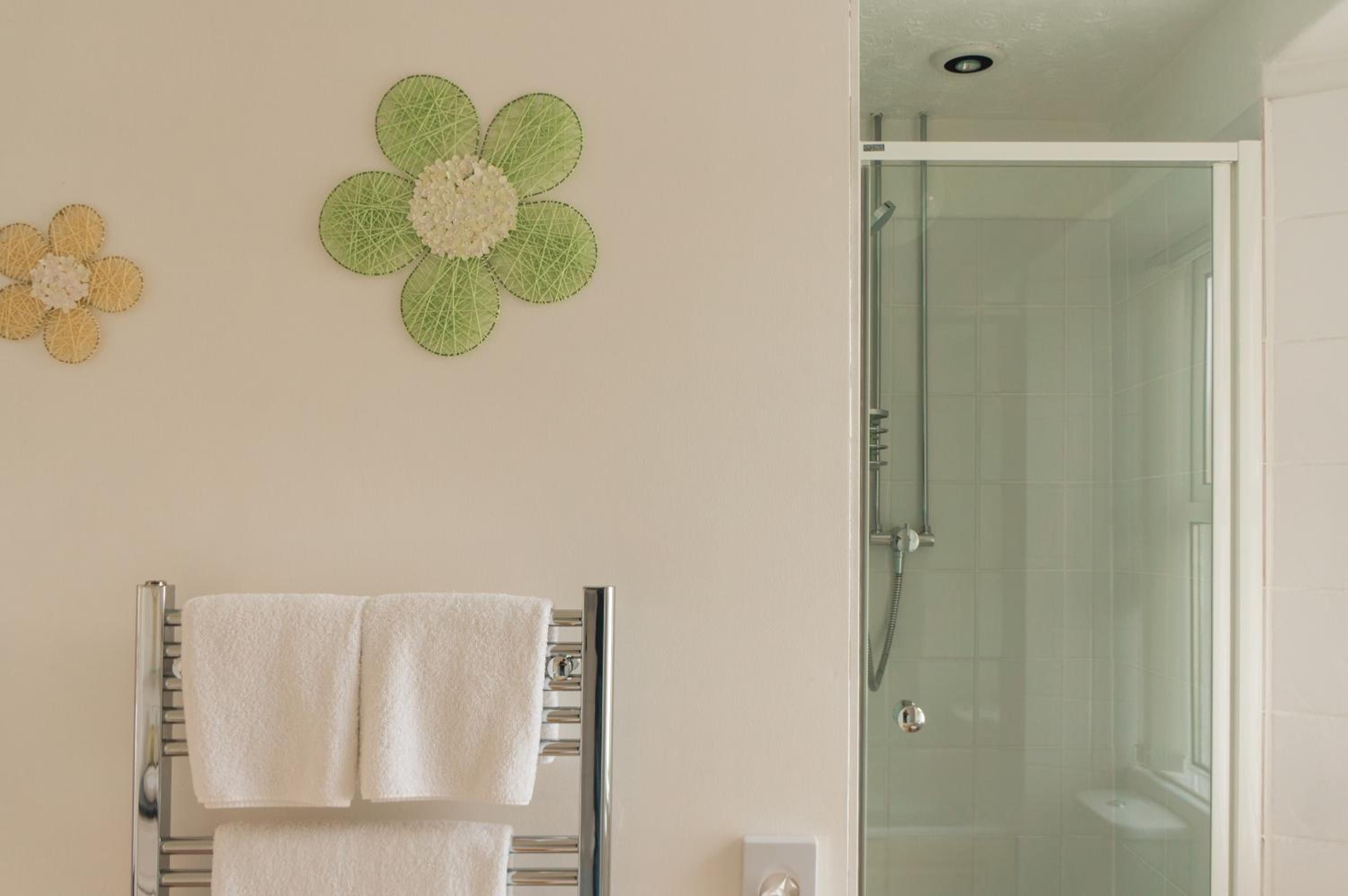 A bathroom with a glass shower door, a towel rack with two towels, and two wall-mounted flower decorations.