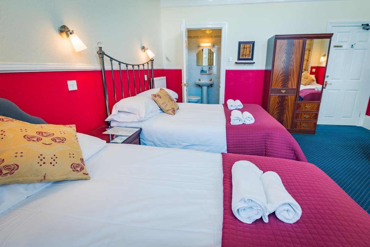 A hotel room with two beds, a wardrobe, a bathroom, and a mirror.