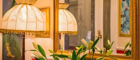 A room with a red wall, a large mirror with a gold frame, and two lamps on a wooden table.