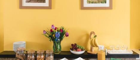 A breakfast buffet with various food items, a vase of flowers, and framed pictures on the wall.