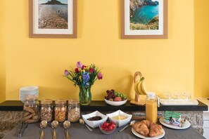 Um buffet de café da manhã com diversos alimentos, um vaso de flores e quadros nas paredes.