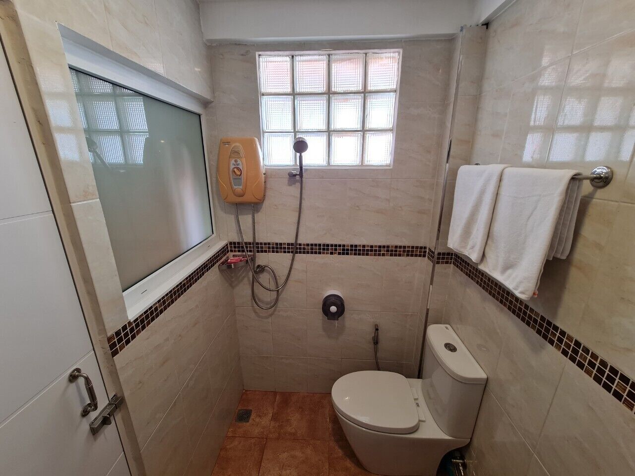 A small, tiled bathroom with a toilet, a shower, and a window.