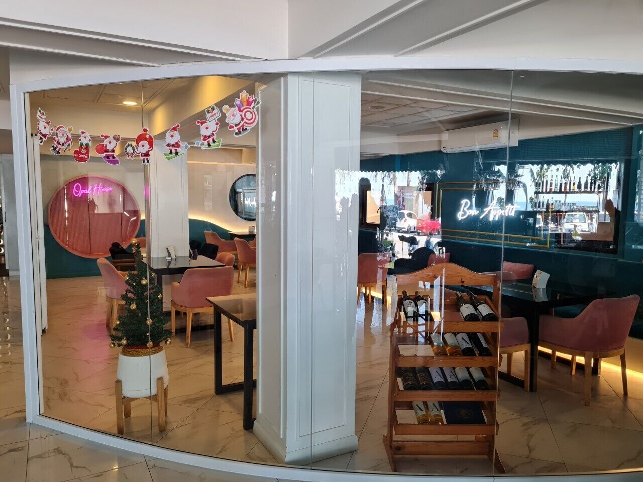 Un restaurante con un árbol de Navidad, sillas rosas y una estantería para vinos.