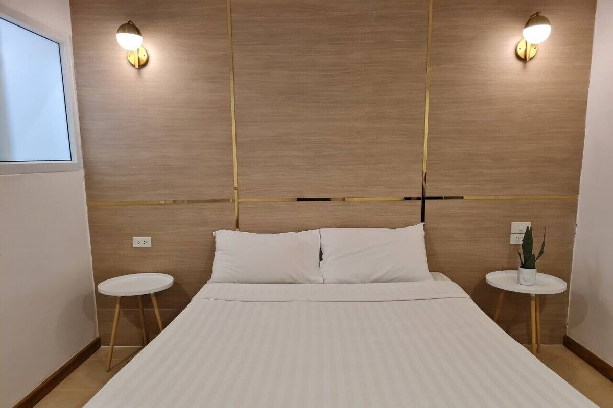 Hotellihuone, jossa on suuri sänky, kaksi yöpöytää, seinään kiinnitetty valaisin ja pieni ruukkukasvi.