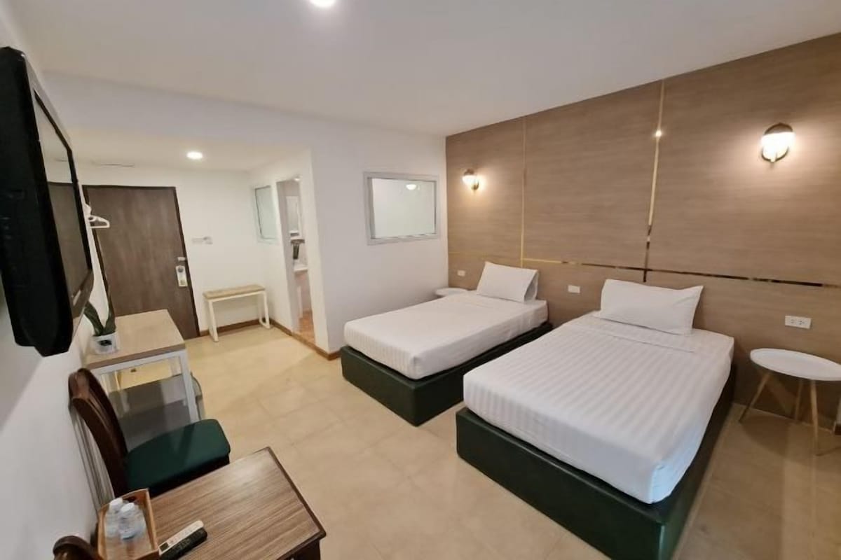 A hotel room with two beds, a desk, a chair, a small table, and a mirror.