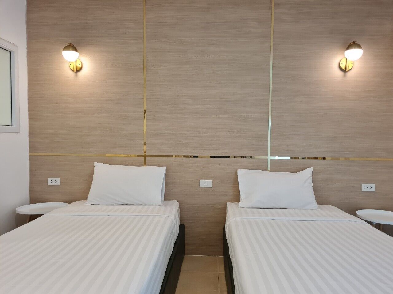 A hotel room with two beds, a wooden headboard, and wall-mounted lights.