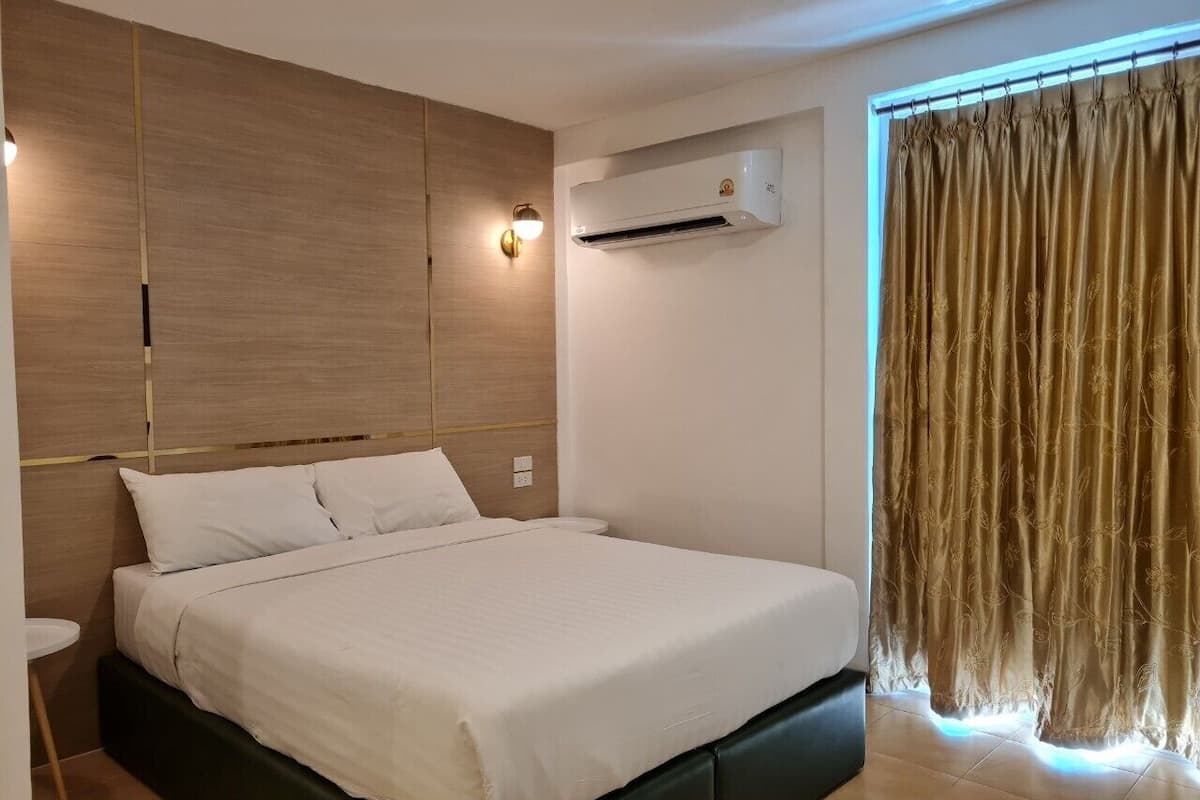 Moderni hotellihuone, jossa on sänky, yöpöytä ja ilmastointilaite.