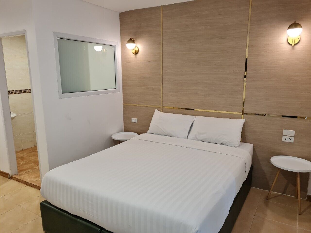 A hotel room with a large bed, a bedside table, a small round table, and a mirror on the wall.