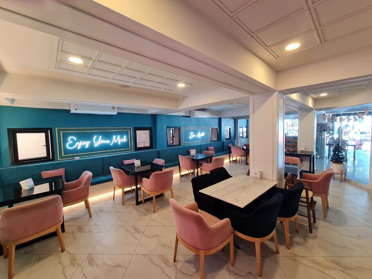 Un restaurante moderno con paredes verde azuladas, sillas rosas y un letrero de neón.