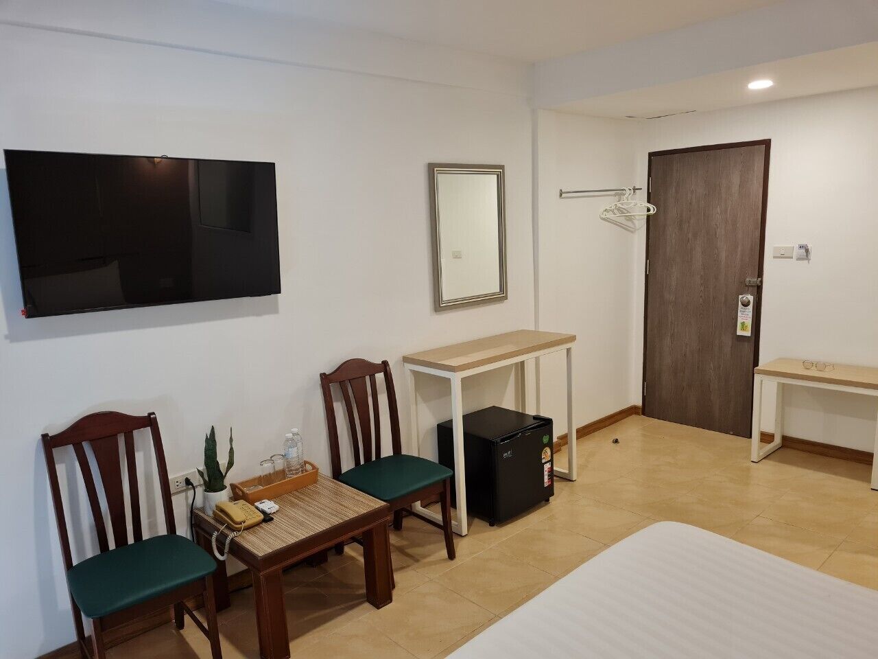 A hotel room with a bed, a desk, two chairs, a small table, a TV, a mirror, a door, and a trash bin.