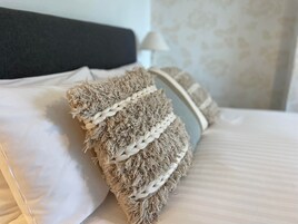 Una cama con sábanas blancas y un cojín beige con textura.