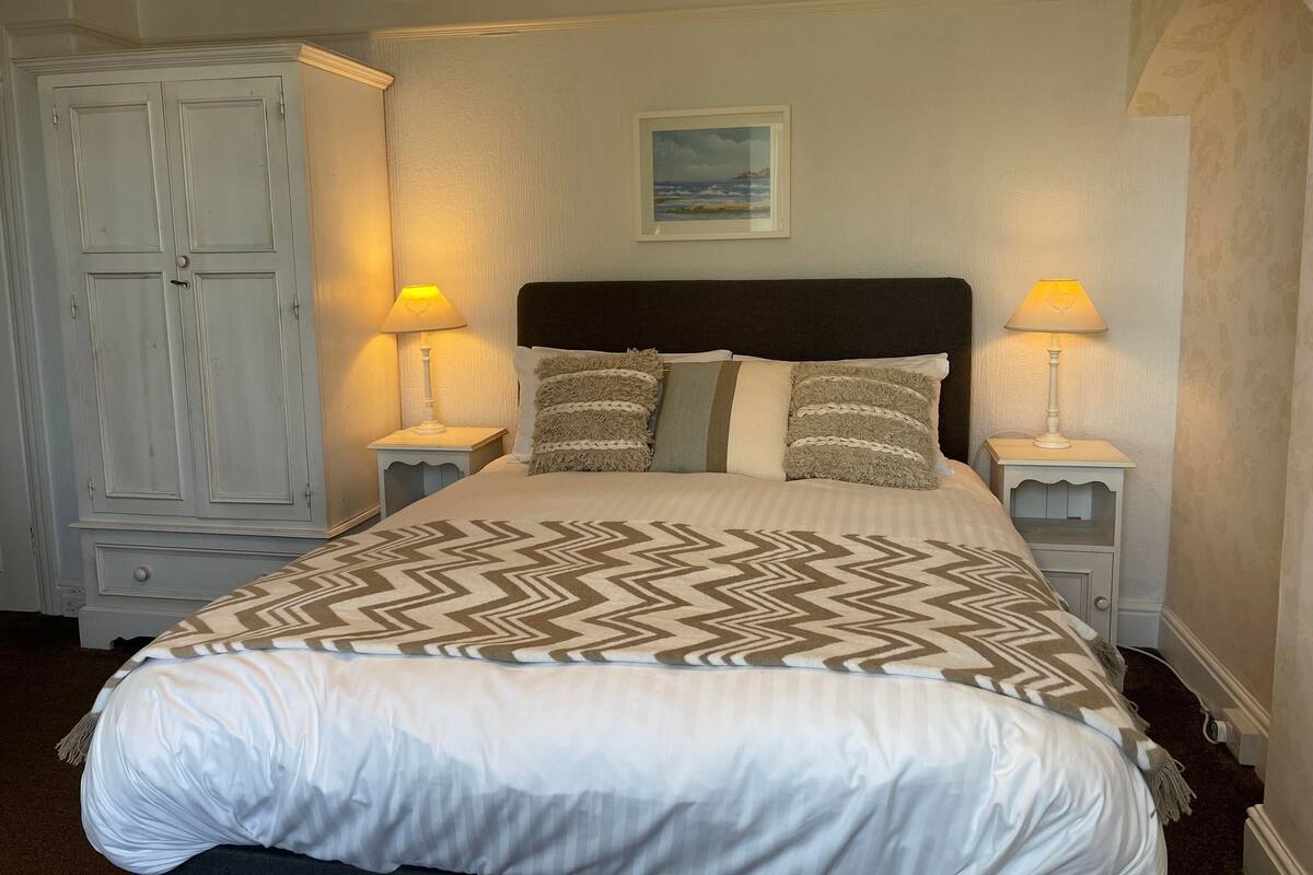 A neatly made bed with a patterned bedspread, two bedside lamps, and a painting on the wall.