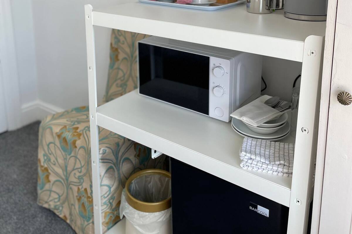 A hotel room with a white minibar, a television, and a small seating area with a patterned cushion.
