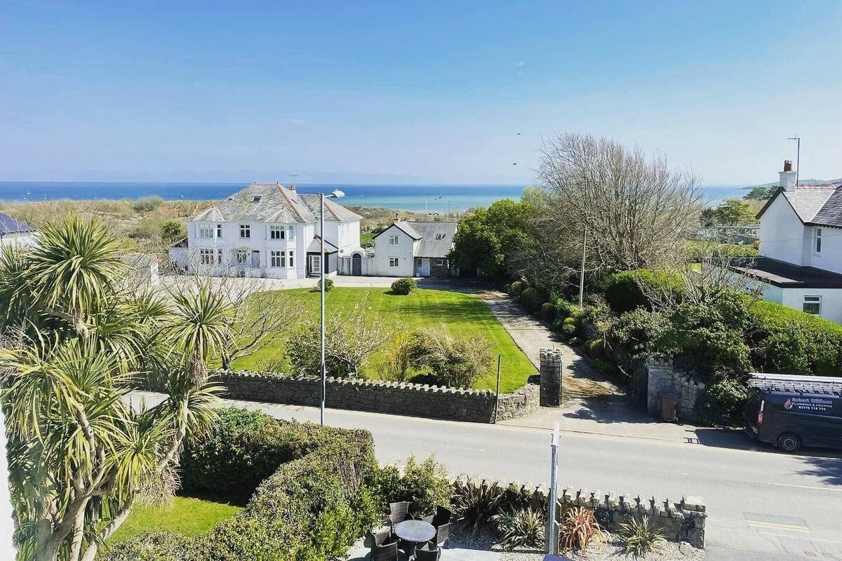 A coastal residential area with a large white house, a smaller attached building, and a view of the sea.