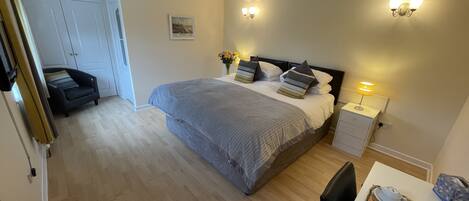 A bedroom with a bed, bedside table, lamp, and a small table with items on it.