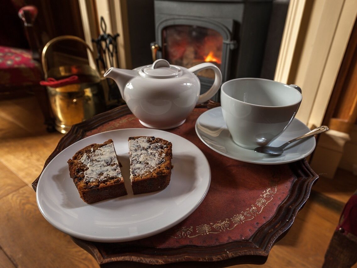 A tray with a slice of cake, a teapot, and a cup on a table near a fireplace.