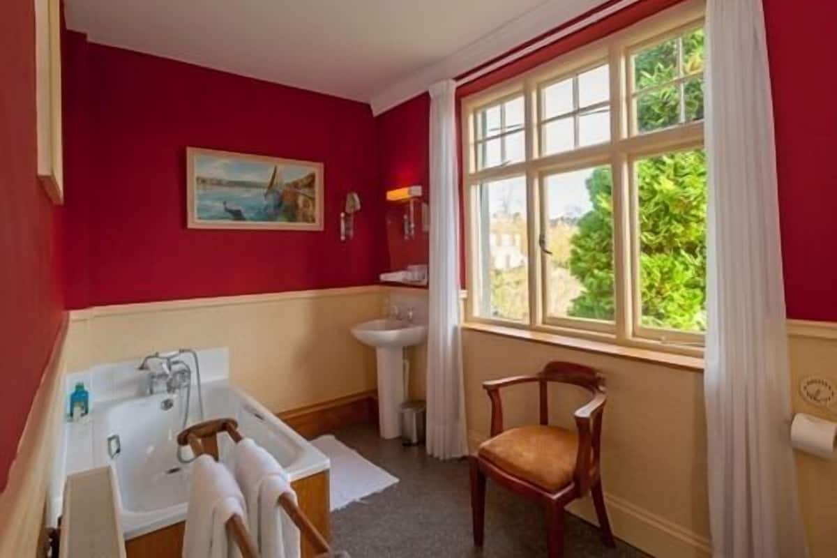 A bathroom with a bathtub, sink, and chair near a window with a view of greenery.