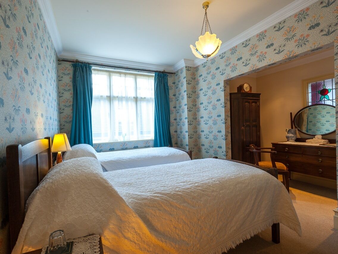Habitación de hotel con dos camas, un tocador, un espejo y una ventana con cortinas.