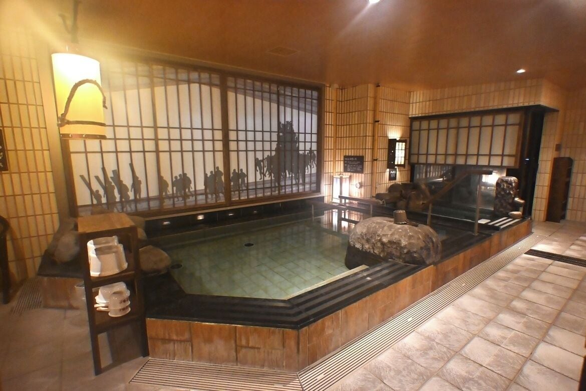 Ett traditionellt japanskt rum med tatamimattor på golvet, en receptionsdisk i trä, ett stort fönster med utsikt och en fontän av sten.
