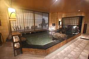 Una habitación de estilo japonés tradicional con suelo de tatami, un mostrador de recepción de madera, un ventanal con vistas y una fuente de agua de piedra.