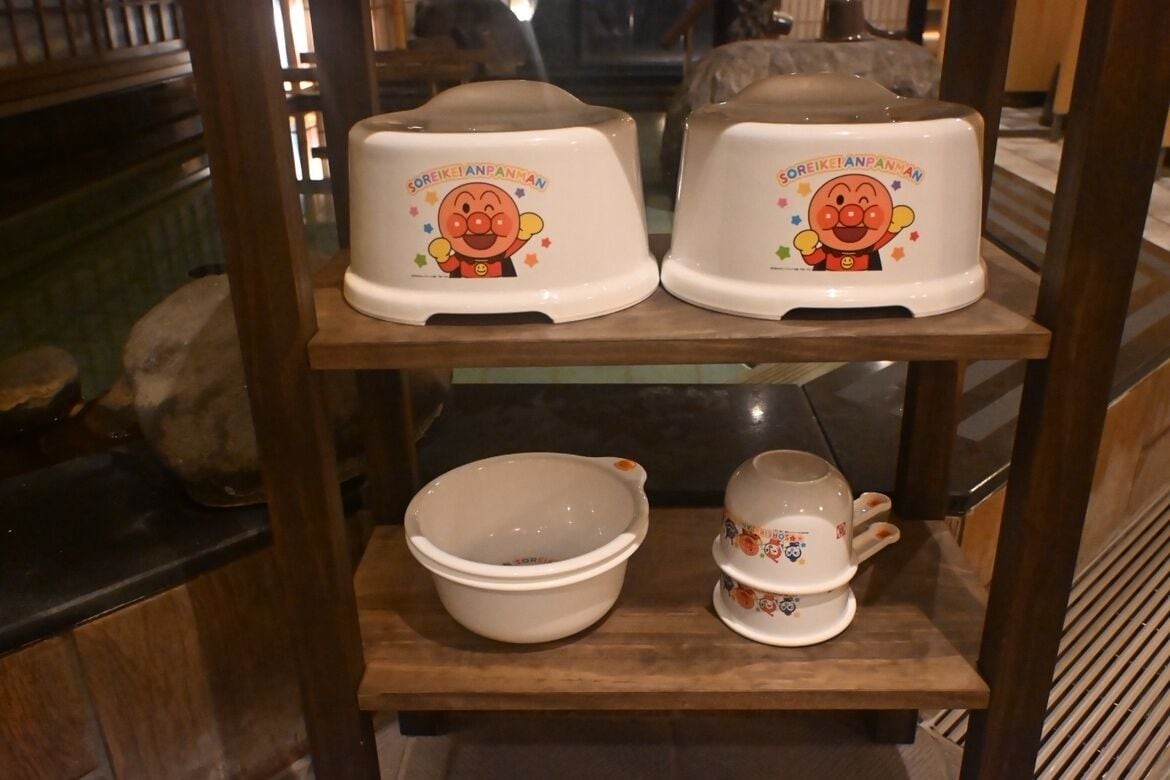 A shelf with two white ceramic containers with cartoon characters and text, a white ceramic bowl, and a matching cup.