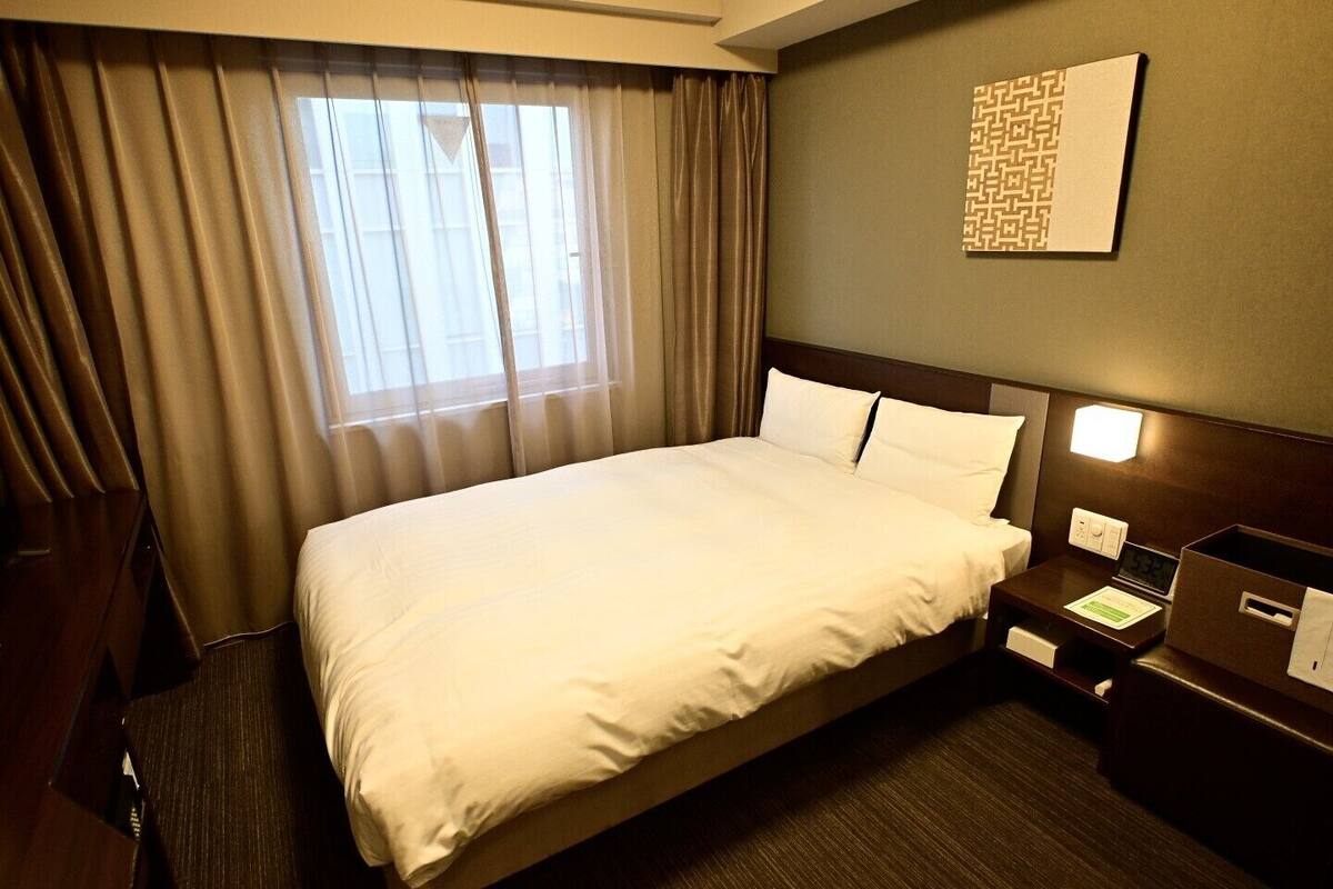A hotel room with a large bed, a nightstand, a desk, and a window with curtains.