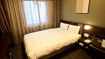 A hotel room with a large bed, a nightstand, a desk, and a window with curtains.