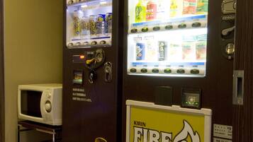 A vending machine with a Kirin logo and a fire symbol, located next to a microwave and a metal rack.