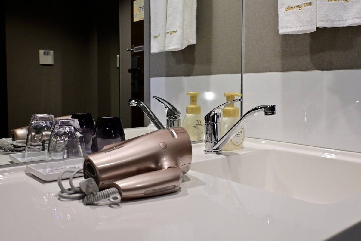 A bathroom with a sink, two faucets, and a mirror. There are towels hanging on the wall and a hairdryer on the counter.